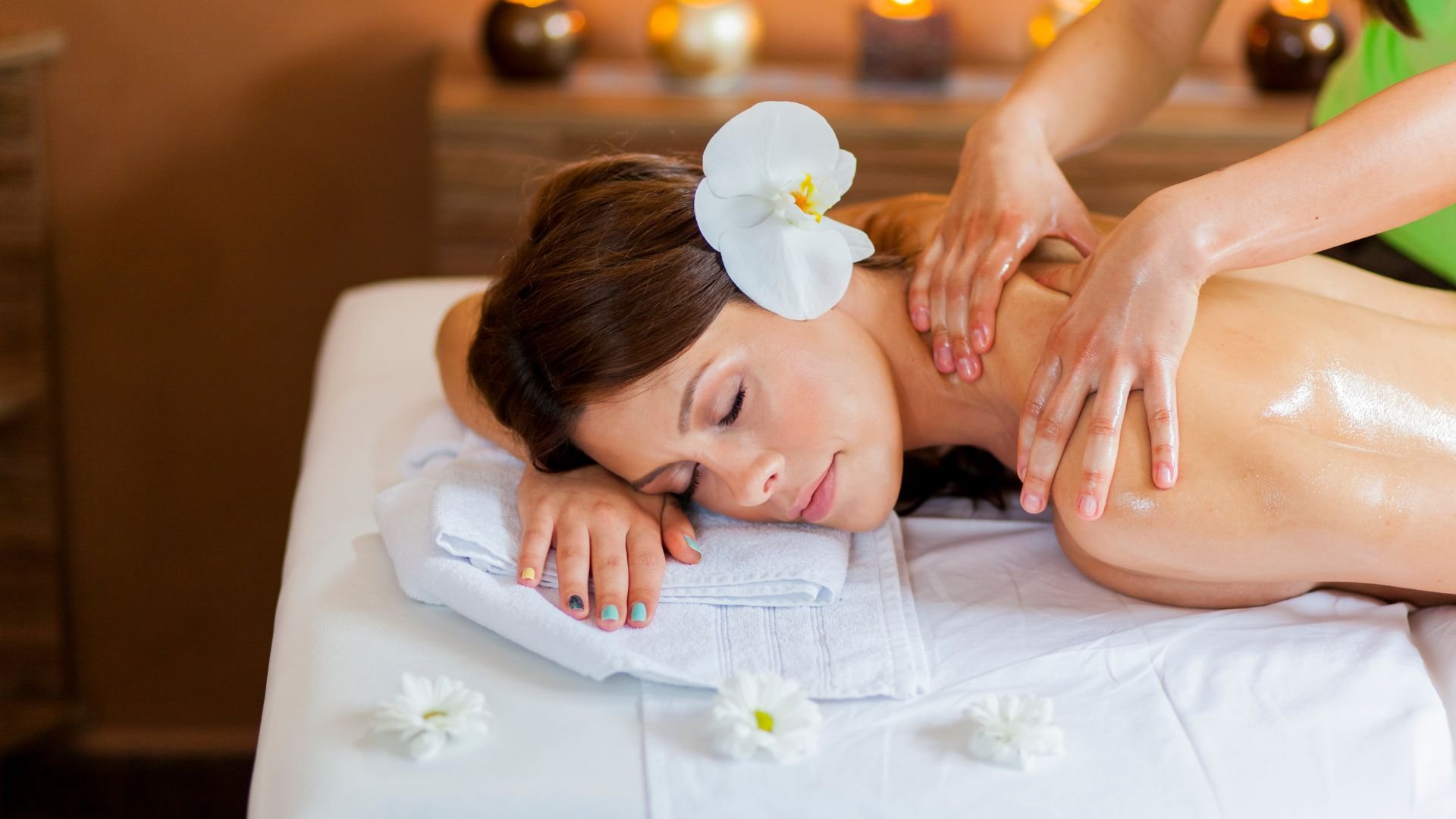 Relaxing spa massage with white orchid, candles, and massage therapist's hands