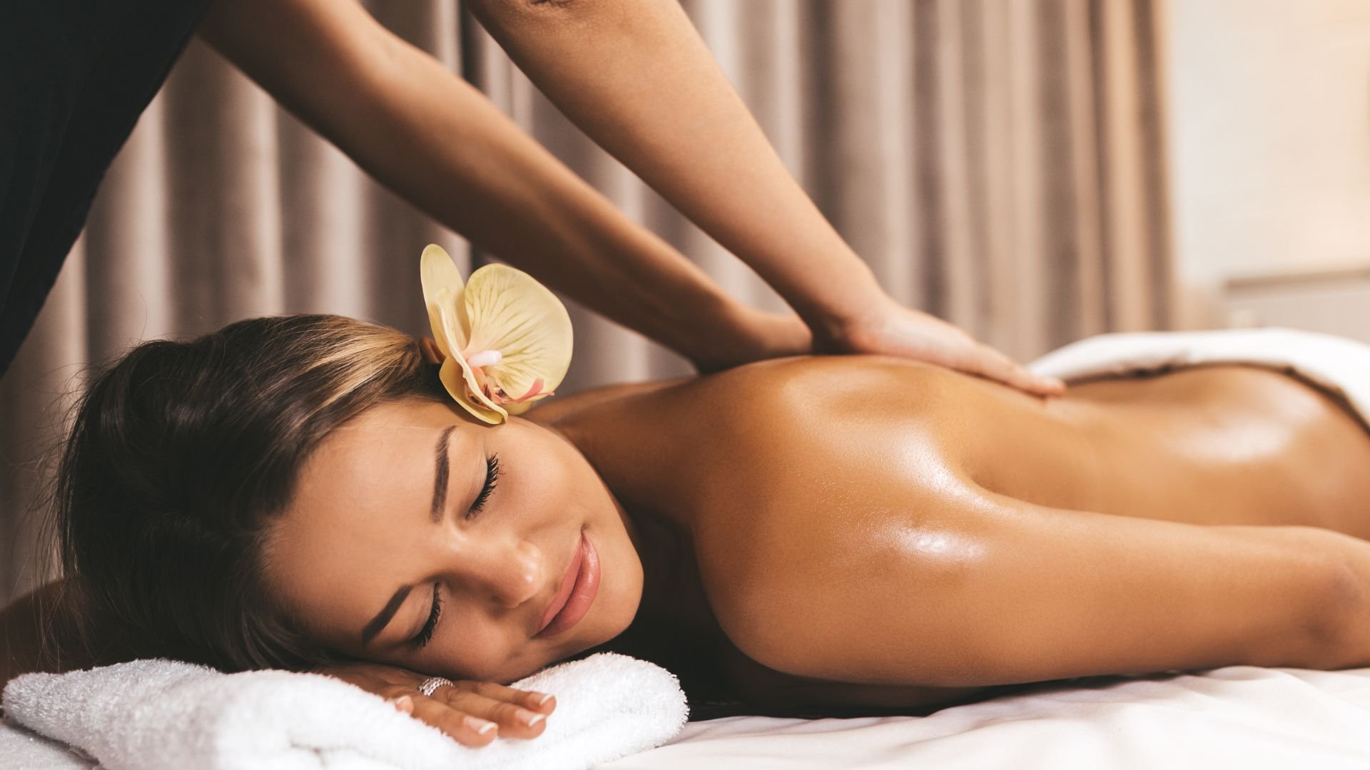 Relaxed person receiving massage with orchid, lying on white towel